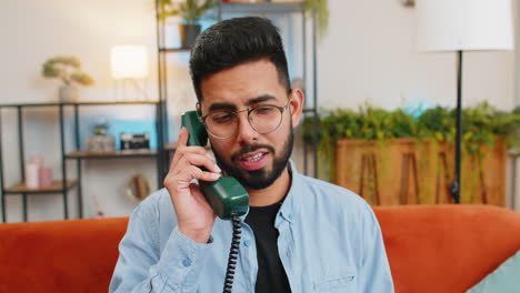 hombre indio irritado hablando por teléfono con cable vintage conversación aburrida con línea directa en casa