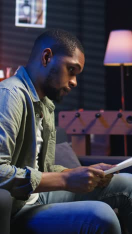 vertical video young adult sitting on couch and reading research papers with analytics