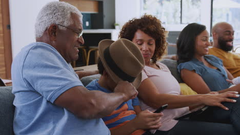 multi-generation african american family relaxing at home sitting on sofa watching tv together