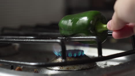 mano pone pimiento verde entero en la estufa con fuego bajo para asar