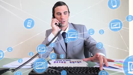 Animation-of-network-of-digital-icons-over-caucasian-businessman-talking-on-phone-and-using-computer