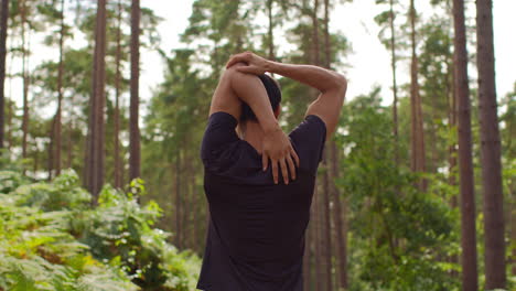 rear view of man warming up and stretching arms before work out exercising running through forest