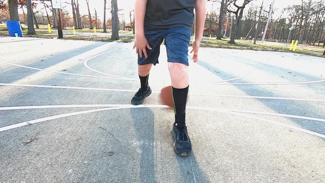 Un joven adolescente demostrando sus habilidades de regateo de baloncesto en una cancha de cemento de un parque de la ciudad.