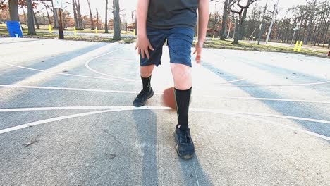 a young teenage boy displaying basketball dribbling skills on a concrete playground basketball court in a city park