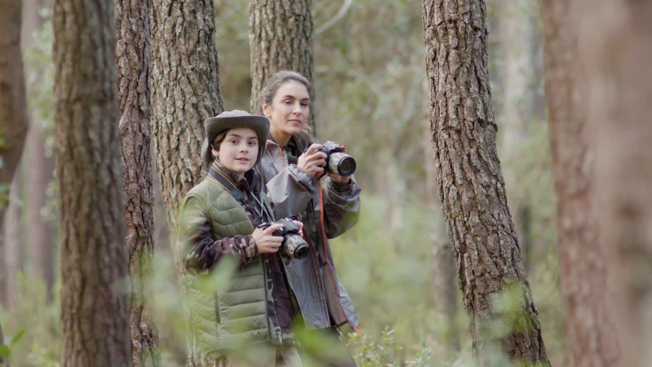 exploradora de la naturaleza femenina y su hijo caminando en el bosque con cámaras