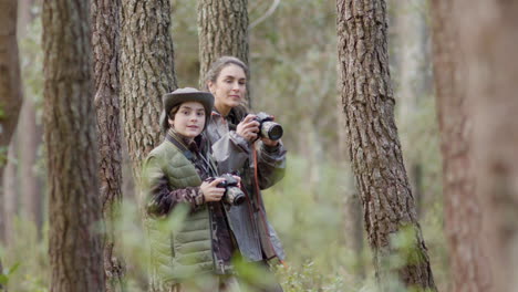 female nature explorer and her son hiking in forest with cameras