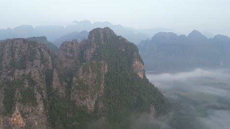 drone shot of dramatic cliffs above foggy valley in vang vieng, the adventure capital of laos