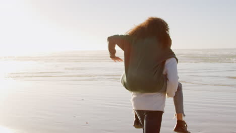vista trasera del hombre dando a la mujer a cuestas en las vacaciones de playa de invierno