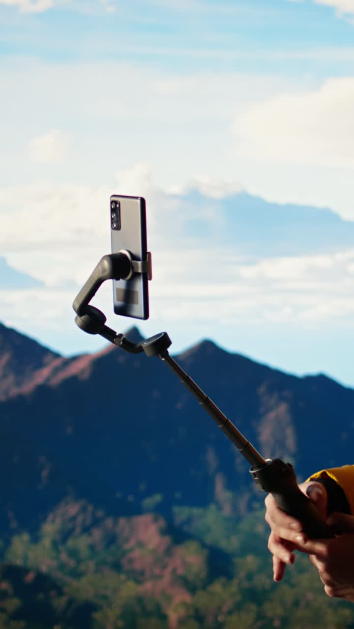 Mand vlogger med smartphone og selfiestang i bjergene