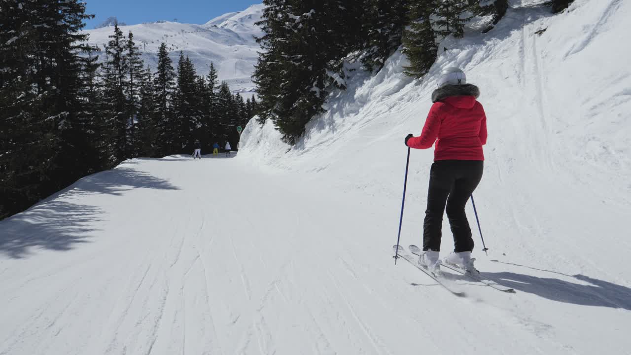 Sciatrice vista di spalle in movimento che scende su una pista da sci tra una pineta