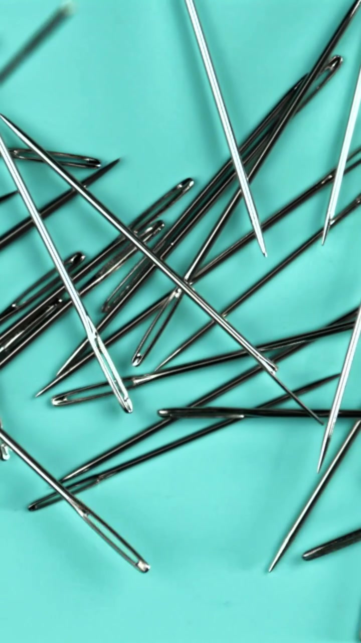Metallic Sewing Needles Falling and Scattering on Turquoise Background