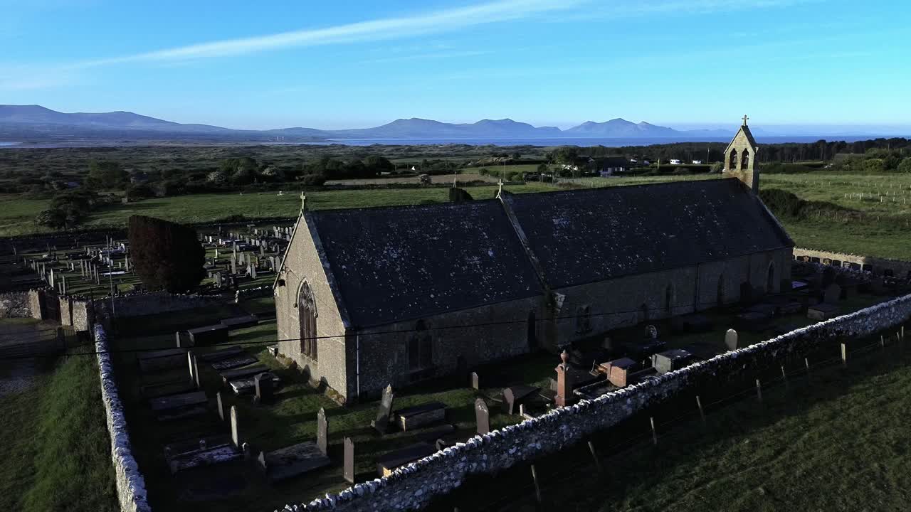 St Peters church in rural Newborough aerial view orbiting Welsh slate gravestones at sunrise