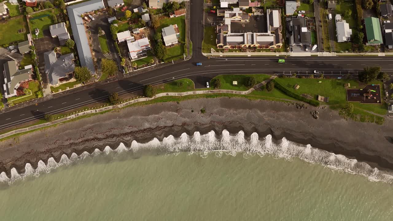 Driving cars on coastal road near stony beach of Kaikoura, New Zealand. Aerial top down shot. Noble houses and homes in small town