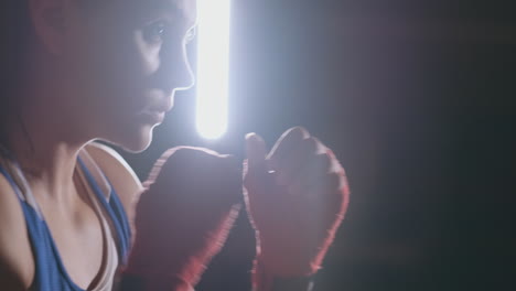 a beautiful woman boxer trains in a dark gym and works out punches in slow motion. side view. steadicam shot