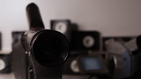 Close-up-of-Old-Black-Camcorder-lens-with-grey-camcorder-and-tapes-in-background