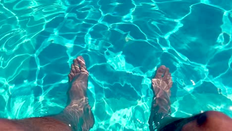 hombre sentado en el borde de la piscina pateando los pies bajo el agua en agua azul clara ondulada