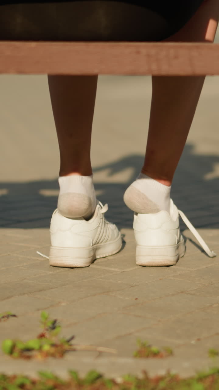 벤치에 앉아 롤러 스케이트를 착용하기 위해 손을 는 동안 색 스니커에서 부분적으로 나온 여자의 다리의 뒷면, 빛은 보행길에 부드러운 그림자를 던집니다.