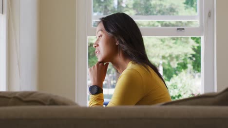 Side-view-of-thoughtful-biracial-woman-sitting-and-looking-outside-window