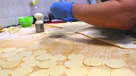 woman cuts round pieces from raw dough to make dumplings