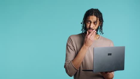 Man-inputting-data-on-laptop-while-standing-in-blue-studio-background