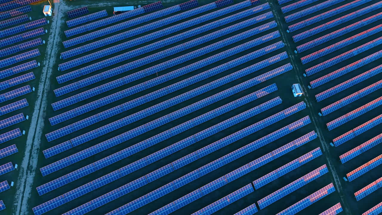 Vista aerea di un impianto di pannelli solari alla luce del tramonto. Prospettiva dall'alto di un parco fotovoltaico durante l'ora d'oro con ombre lunghe e illuminazione calda