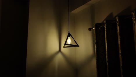 Triangle-lamp-hanging-down-the-wall-in-a-room-with-curtains,-defensive-yellow-light,-static-shot-in-a-room