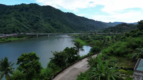 Overhead-Drone-Shot-of-Riverside-Colonial-Church,-revealing-lush-tropical-valley-with-vast-river,-long-bridge-and-jungle-covered-hills