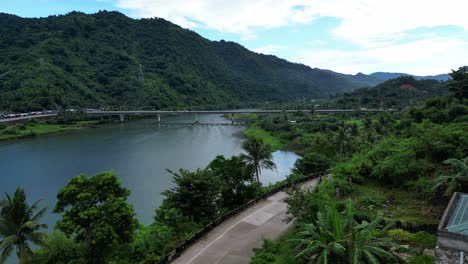 overhead drone shot of riverside colonial church, revealing lush tropical valley with vast river, long bridge and jungle-covered hills