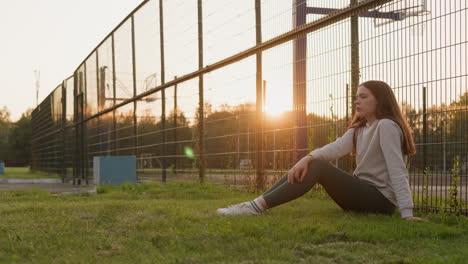 young woman sits on grass in fading sunset. grappling with feelings of loneliness and frustration during challenging and disheartening moment of woman life