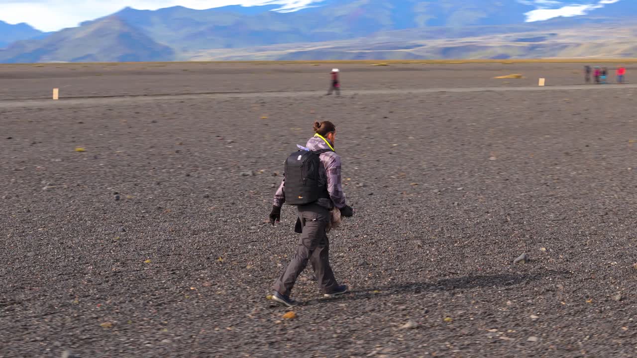 Rotazione del drone attorno a un turista che cammina nel paesaggio desertico dell'Islanda, equipaggiato con una borsa fotografica.