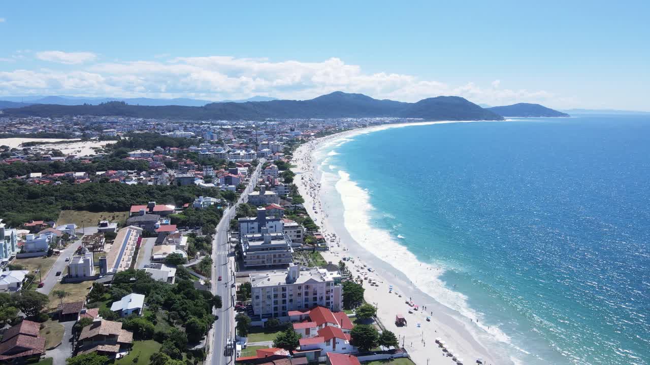 Panoramic aerial view of Ingleses beach in Florianópolis, Santa Catarina, crowded with people and umbrellas during the peak summer season with turquoise blue sea