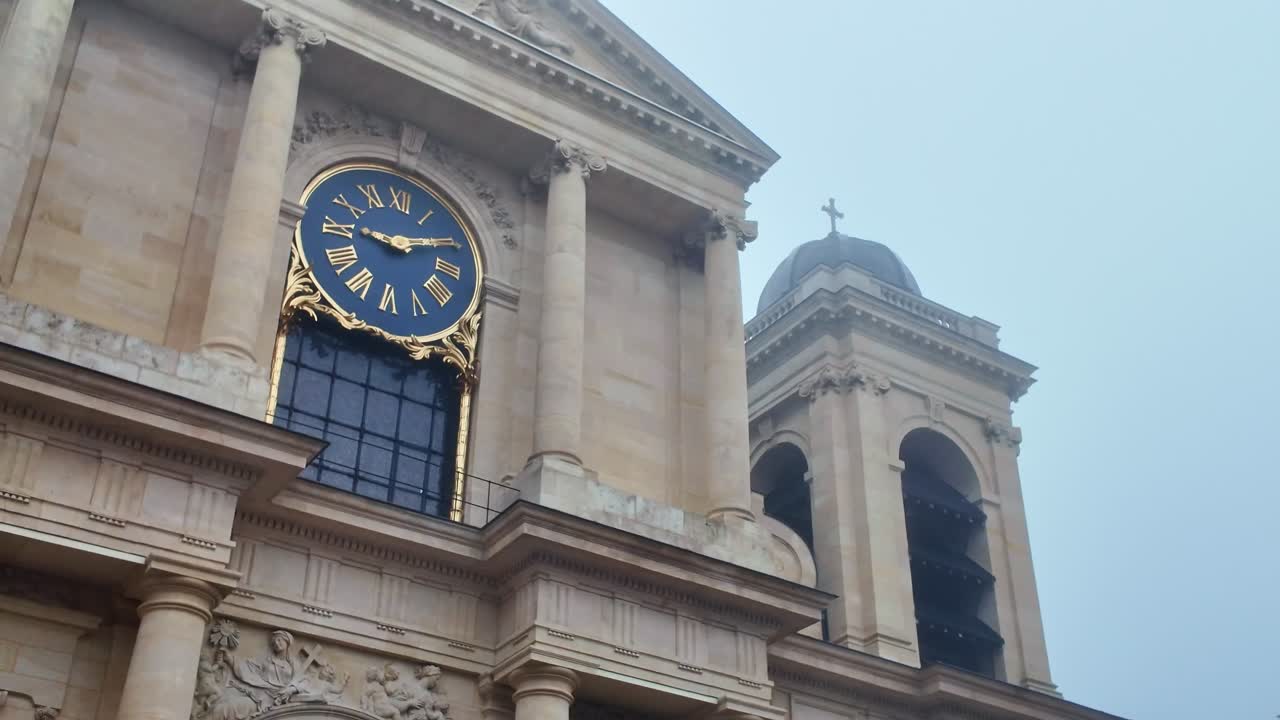 Low-angle view of the neoclassical facade of Notre-Dame de Versailles church. Features a prominent blue clock with gold numerals. Historic religious architecture in France