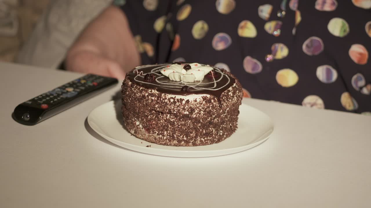 Senior woman watching television and eating cake in a dark room