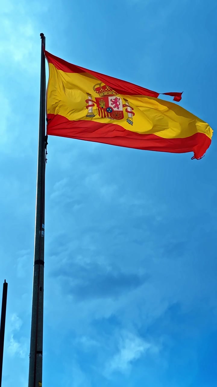 Bandiera nazionale della Spagna che sventola sull'asta. La bandiera spagnola rossa e gialla con lo stemma che sventola al vento contro un cielo blu nuvoloso