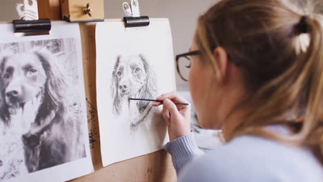 Female-Teenage-Artist-Sitting-At-Easel-Drawing-Picture-Of-Dog-From-Photograph-In-Charcoal