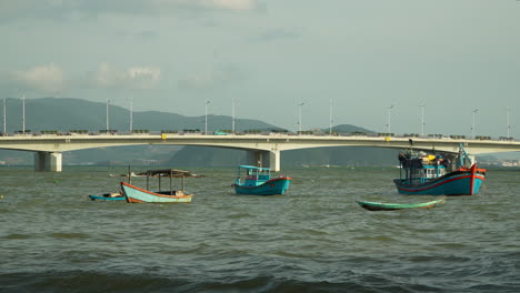 Wooden-fishing-boats-anchor-on-Cai-River-water-at-Cu-Lao-village-coast-with-Tran-Phu-Bridge-and-Mountains-in-Background,-Nha-Trang-Vietnam