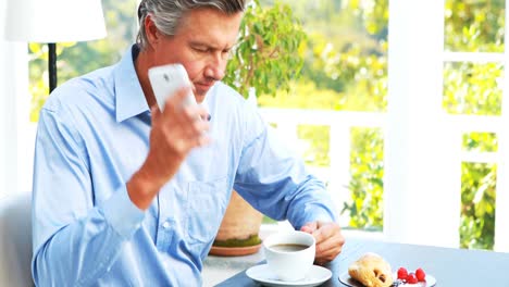 Businessman-talking-on-mobile-phone-and-drinking-coffee-in-restaurant