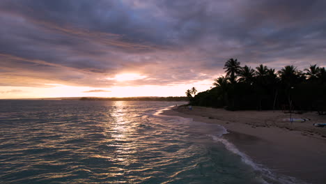 Aerial-drone-shot-alone-sandy-beach-with-Caribbean-Sea-during-stunning-golden-sunset-behind-cloudscape