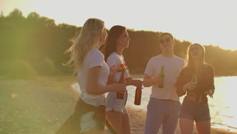 un grupo de estudiantes celebra el final del semestre con cerveza en la playa. están bailando y bebiendo cerveza en una fiesta al aire libre al atardecer en la noche de verano.