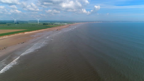 Establishing-Aerial-Drone-Shot-Over-Fraisthorpe-Beach-on-Sunny-Day-with-Wind-Turbines-in-the-Background-Yorkshire-UK-East-Coast