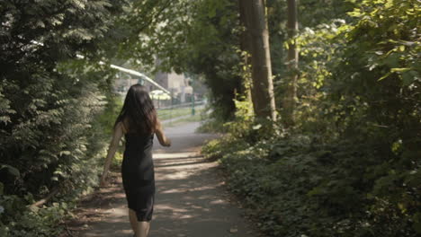 Plano-General-De-Una-Hermosa-Mujer-Asiática-Vestida-De-Negro-Caminando-Felizmente-Por-Un-Bosque-Soleado,-En-Cámara-Lenta