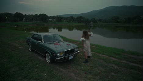 woman by vintage car near a lake at dusk