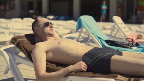 Bald-married-Italian-man-is-lying-on-the-beach-on-deck-chair-sunbathing