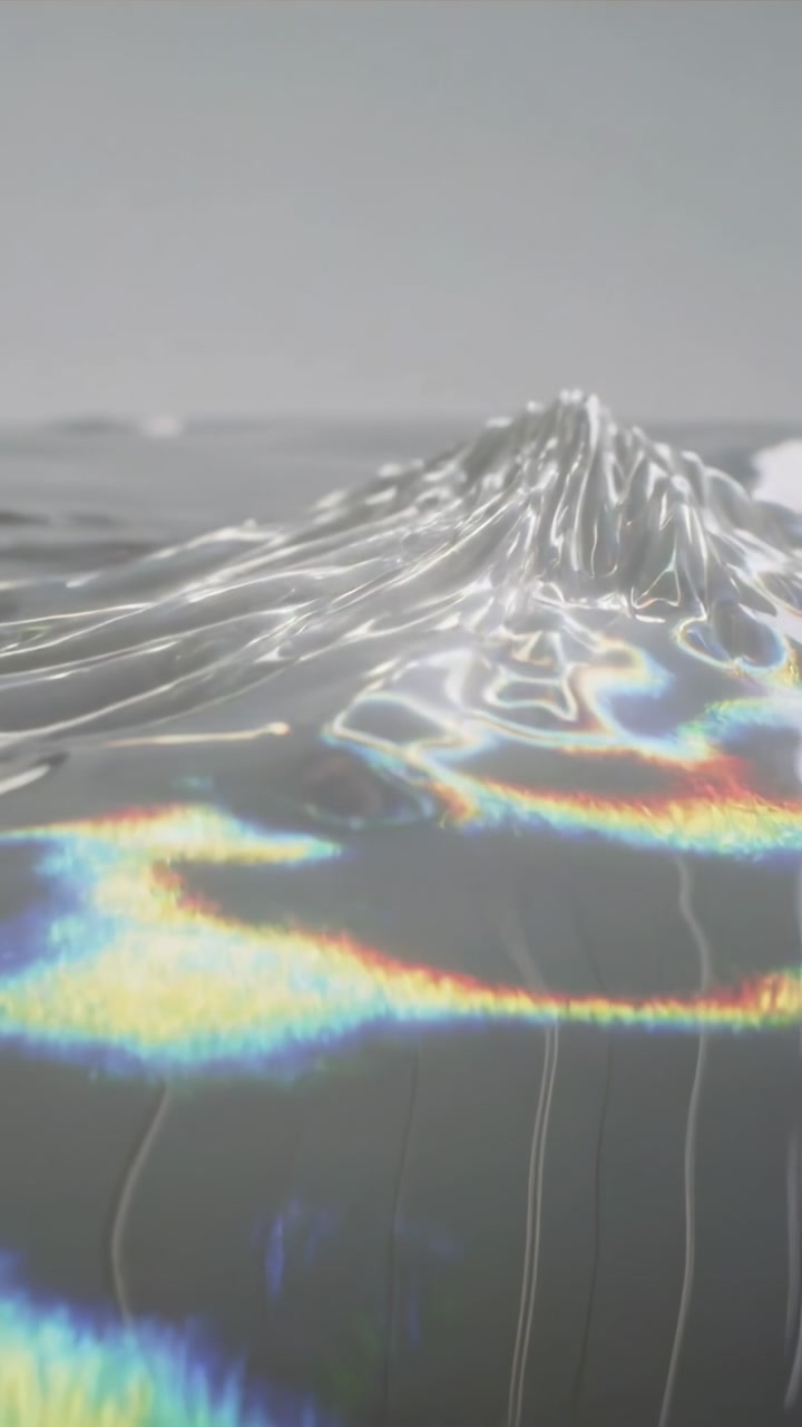 Vertical video: Forming glossy liquid crest responding to light in studio, revealing iridescence