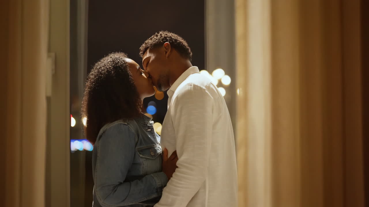 A couple shares an intimate kiss by a window at night