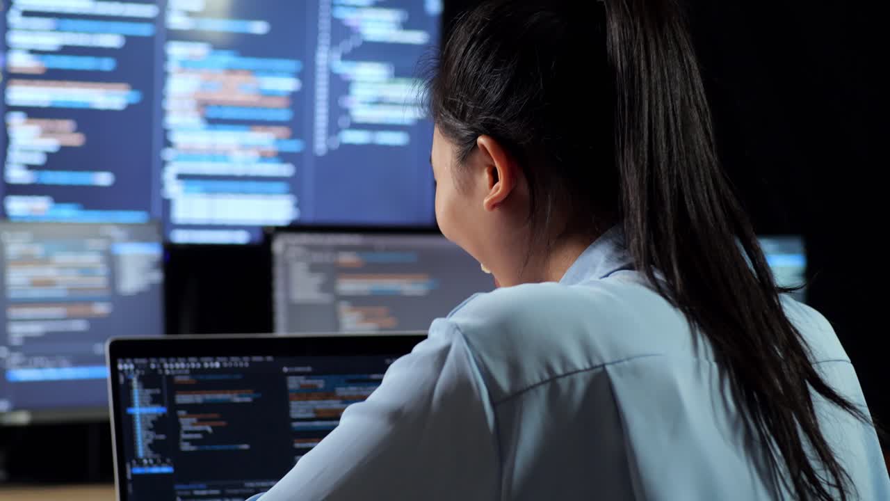 vista de cerca de atrás de una programadora asiática celebrando el éxito de escribir código por una computadora portátil utilizando múltiples monitores que muestran la base de datos en terminales ventanas de escritorio en la oficina