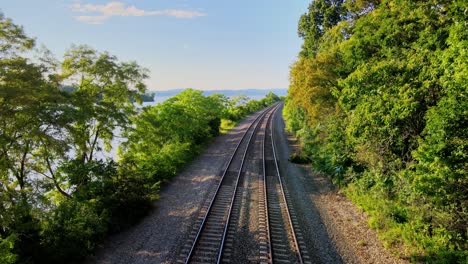 Aerial-drone-footage-of-the-metro-north-Hudson-Line-train-tracks-during-summer-next-to-the-Hudson-river-between-beacon-and-cold-spring,-new-york,-usa