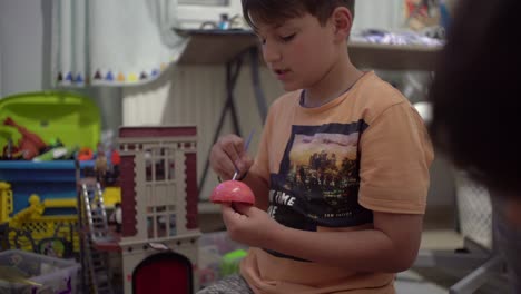 medio, toma estática de un niño caucásico de 8 años, pintando un planeta juguete en su habitación, 4k enfoque selectivo profundidad de campo poco profunda