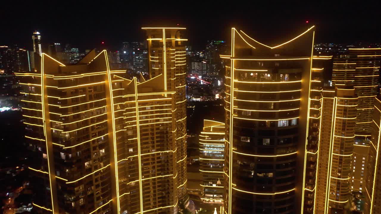 Aerial footage of Rockwell Center skyscrapers and rooftops in Makati, Metro Manila, glowing with lights at night and surrounded by the vibrant energy of the city skyline.