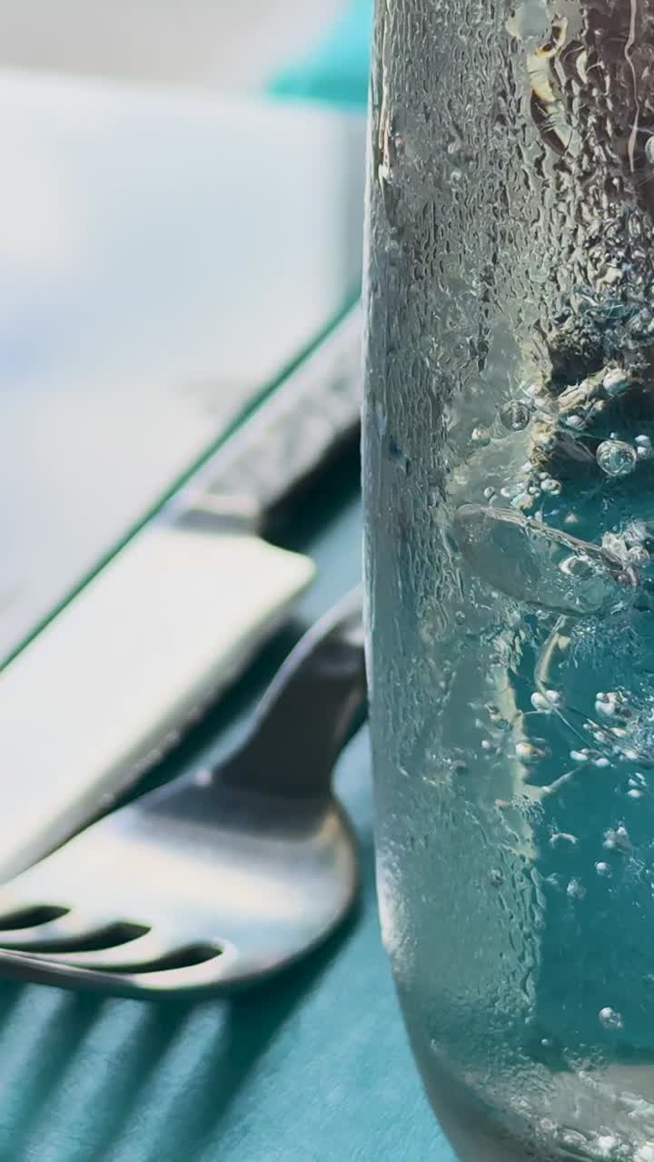 클럽 소다 거품이 유리잔에 상승하는 매크로 뷰, 자연 빛에서 식탁과 식구에 맞춰 설정